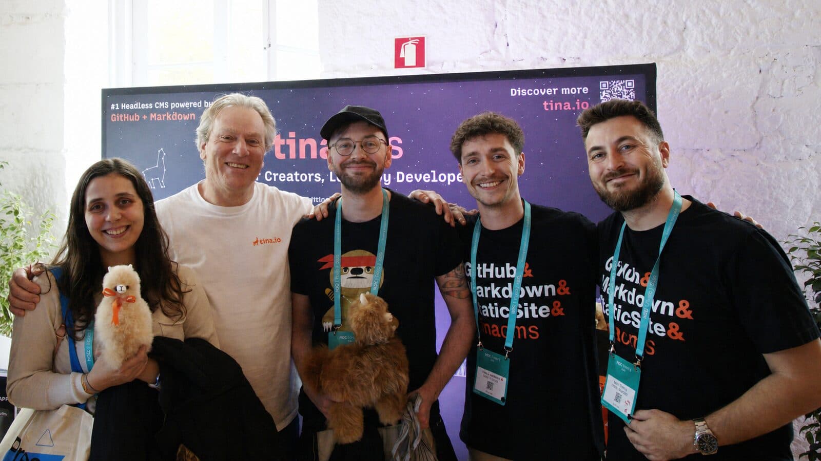 The TinaCMS team holding plush alpacas in front of a tina.io banner at a conference